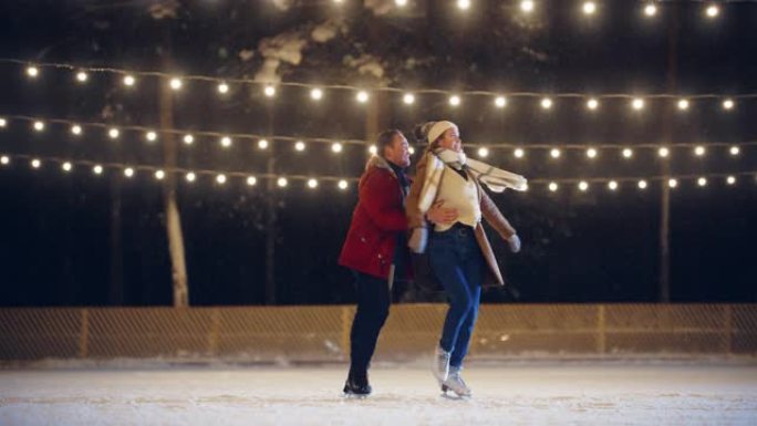 浪漫的冬天下雪的夜晚: 滑冰夫妇在溜冰场上玩得开心，旋转，跳舞，跳跃。户外双人滑冰。美丽的年轻人拥抱