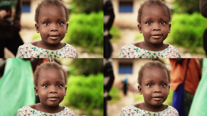 一个可爱的非洲小托德勒看着相机的特写肖像，背景模糊的人在移动。充满纯真和喜悦的黑人孩子，代表着对美好