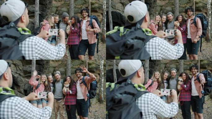 在森林中，多种族的游客为智能手机相机摆姿势，挥舞着双手并亲吻shiba inu狗