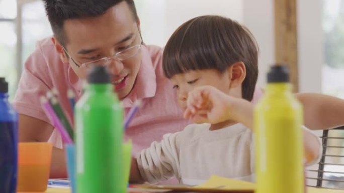 亚洲父亲和儿子在家里的桌子上做手艺很开心