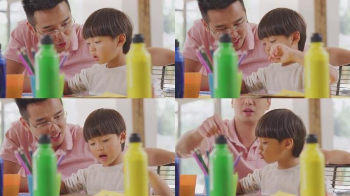 亚洲父亲和儿子在家里的桌子上做手艺很开心