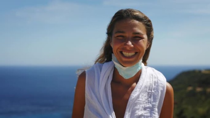 一名年轻女子的真实照片正在脱下防护口罩，在海景背景上深深地呼吸着快乐。