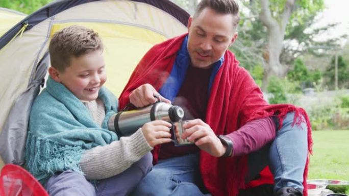快乐的高加索父亲和儿子坐在帐篷里，在花园里喝茶
