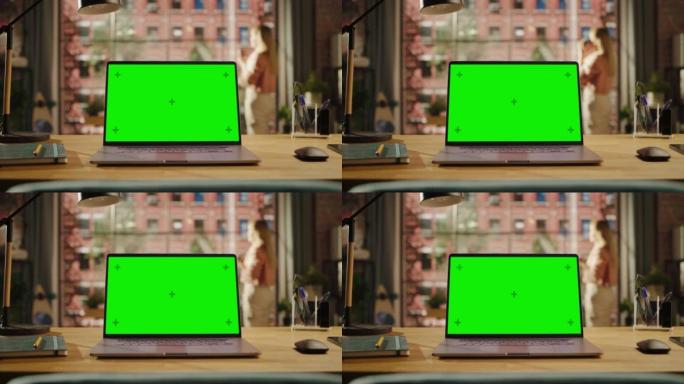 笔记本电脑显示屏，模拟绿屏站在客厅的木桌上。家里或创意阁楼办公室的色度钥匙监视器，背景是女性向外看。