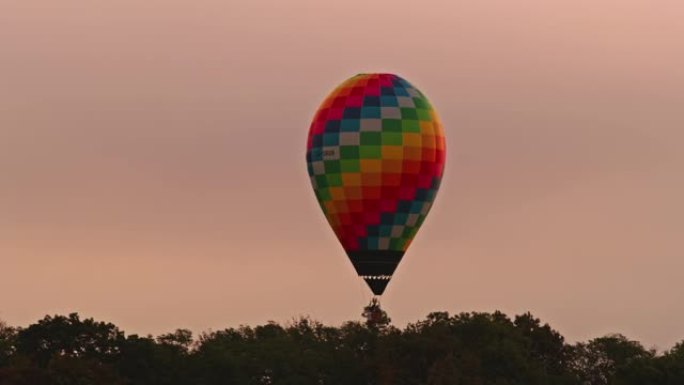 日出时，方格热气球在多云的天空中飞过树木