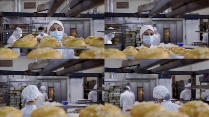在食品加工厂工作的妇女用防护手套取回新鲜出炉的糕点甜点托盘