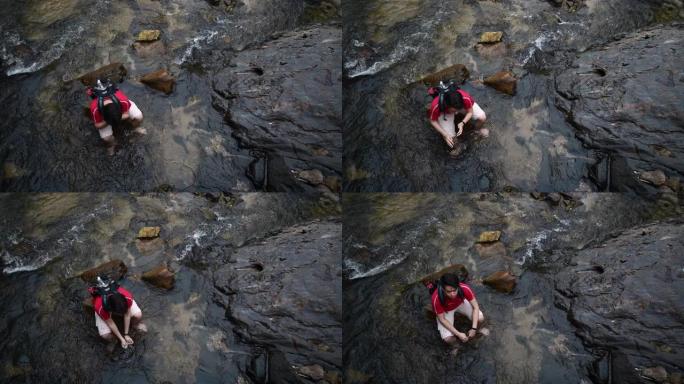 一位亚洲华裔年轻人坐在河中央的岩石上享受