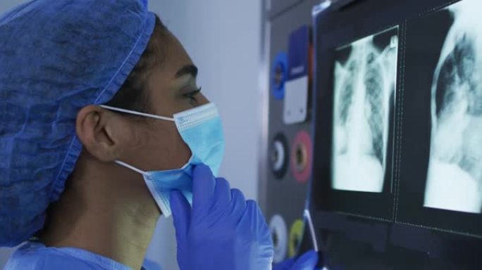 混血女外科医生穿着防护服看着屏幕上的x射线
