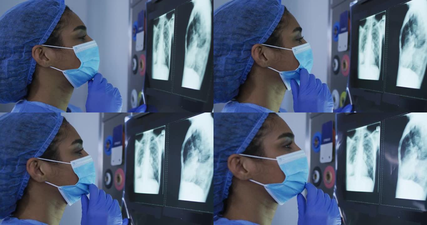 混血女外科医生穿着防护服看着屏幕上的x射线