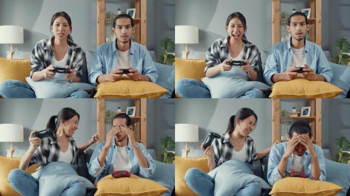 快乐的亚洲年轻夫妇坐在沙发上使用操纵杆控制器玩视频游戏在客厅一起度过快乐的时光。