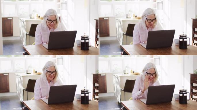在家工作时，戴着眼镜的高级妇女在笔记本电脑上进行视频聊天时挥舞着