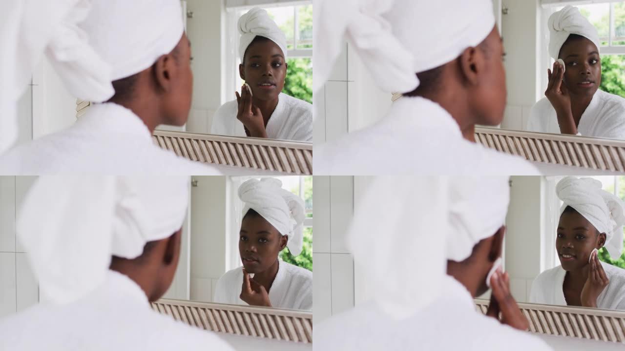 穿着浴袍的非裔美国妇女在照镜子时用棉垫清洁皮肤
