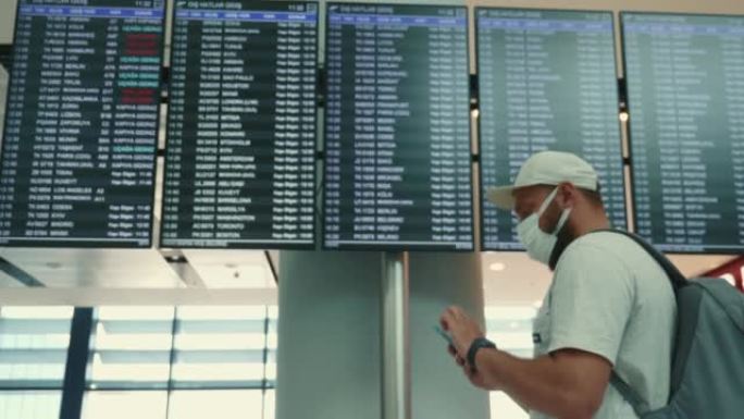 戴着医用口罩的年轻快乐游客在机场航站楼使用智能手机检查时间和航班时刻表。