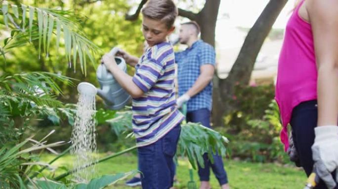 微笑的高加索兄弟姐妹与父母一起园艺，微笑和浇水植物