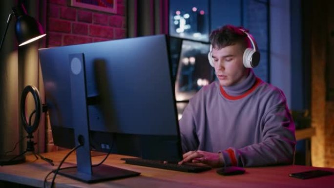 晚上，戴着耳机的年轻帅哥在时尚的阁楼公寓里使用电脑。富有创造力的男性微笑，在家工作，在社交媒体上浏览