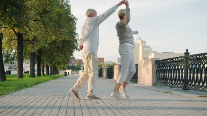 快乐的已婚夫妇的慢动作养老金领取者在城市街道上跳舞微笑着玩乐