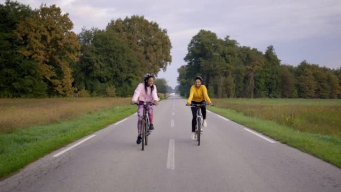 两名成年成年女性的静态手持照片，在高速公路上快乐地骑行，以慢动作穿过相机旁边