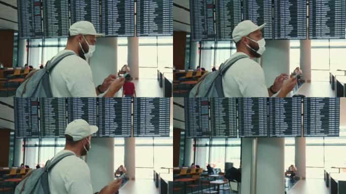 年轻的白人游客戴着口罩，在机场航站楼使用智能手机，检查航班时刻表，走开了。