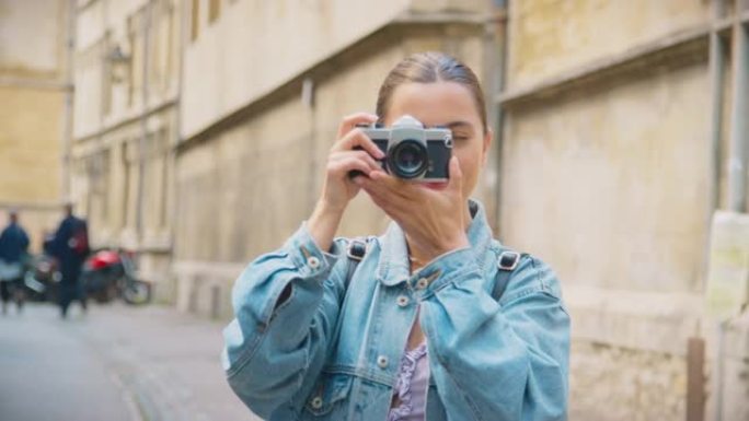 城市街道上的年轻女子在复古数码相机上拍照并发布到社交媒体上