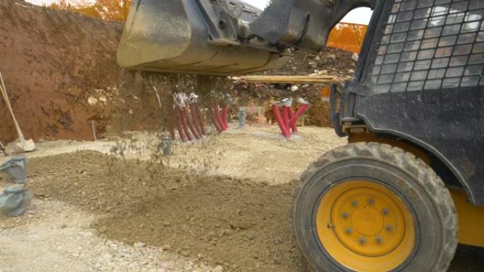 特写: 挖掘机在平整的地面上卸下装满湿砾石的大桶