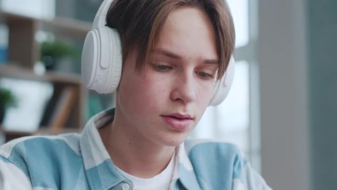 戴着耳机的英俊少年男人在家听音乐特写。迷人的聪明少年放松在音频设备上的歌曲声音。年轻的学生在最喜欢的