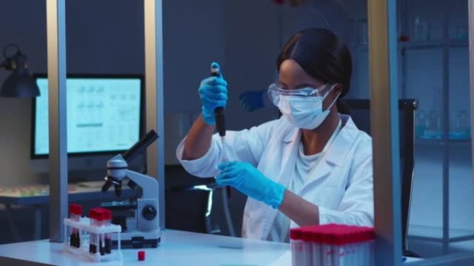 一位年轻的有吸引力的非裔美国女实验室助理戴着防护眼镜，在现代实验室中处理血液样本