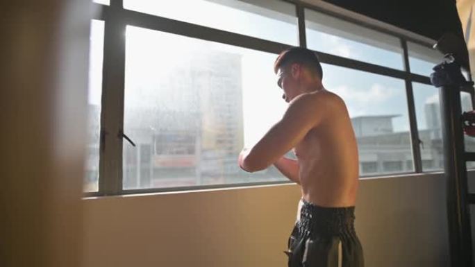 亚洲中国泰拳拳击手系好绷带内运动手套，准备晚上在窗户附近进行拳击训练