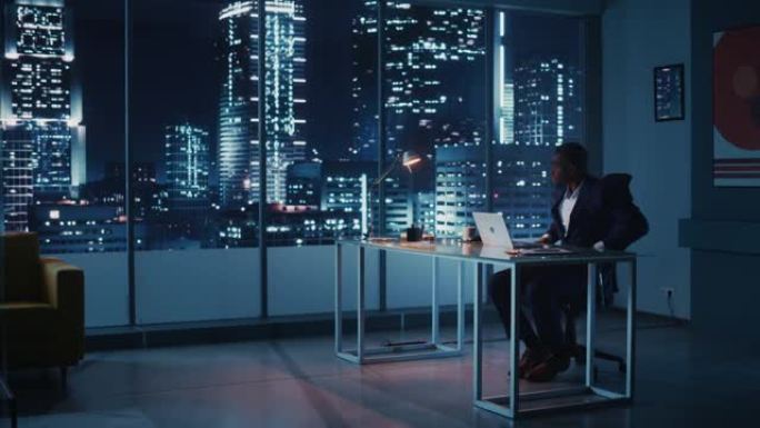 夜间办公室: 成功的黑人商人穿着西装站着，看着窗外的大城市。非裔美国首席执行官对电子商务的环境、社会