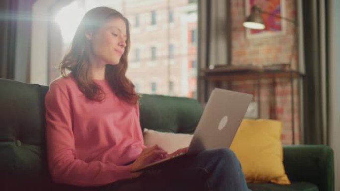 年轻漂亮的女性坐在阁楼公寓的沙发上，在家用笔记本电脑工作。有创造力的女人检查社交媒体，浏览互联网。从