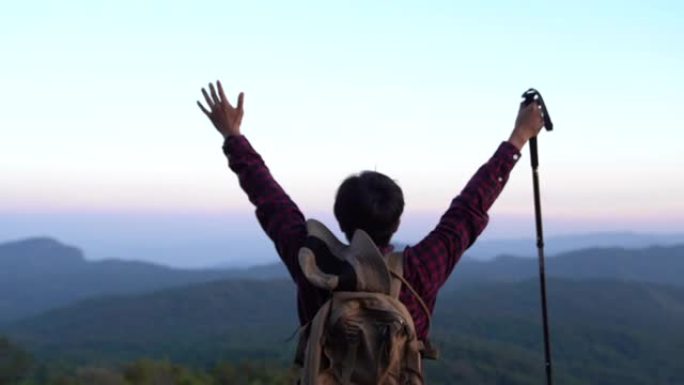 张开双臂的年轻旅行者站在山顶上，欣赏夕阳下的山脉全景。