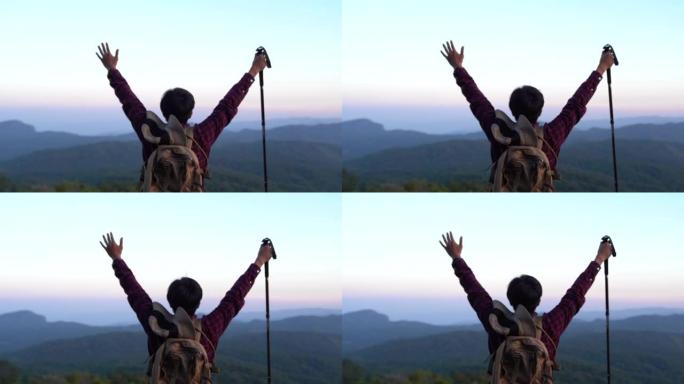 张开双臂的年轻旅行者站在山顶上，欣赏夕阳下的山脉全景。