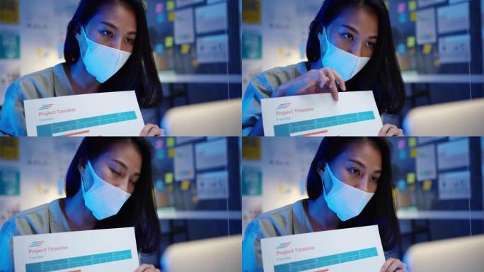 亚洲女商人在新的正常情况下进行社交距离预防，同时在办公室晚上工作时使用笔记本电脑向同事介绍视频通话计