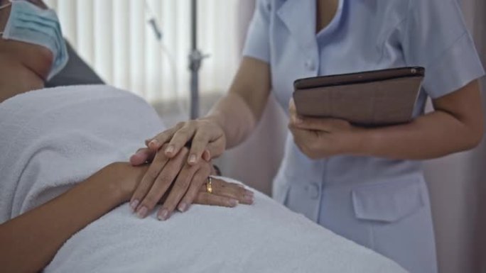 防护面罩中的SLO MO护士在医院病床上触摸病人的手希望，特写