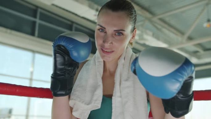 性感的年轻女子戴着拳击手套眨眨眼，独自站在健身房微笑