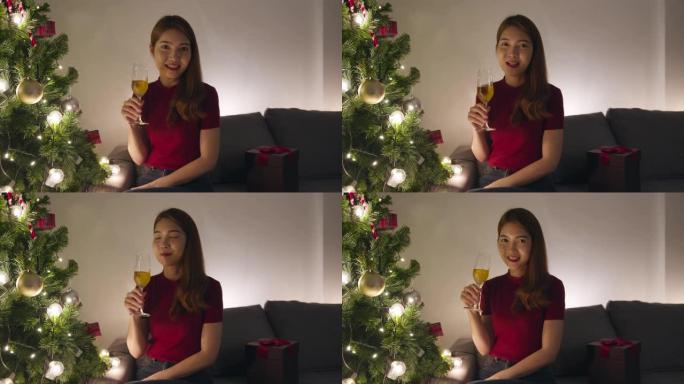年轻的亚洲女性喝酒开心快乐的夜晚派对视频通话与情侣交谈，家里客厅装饰有装饰品的圣诞树。