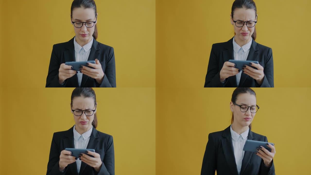 黄色背景下无忧无虑的女商人玩智能手机视频游戏的慢动作