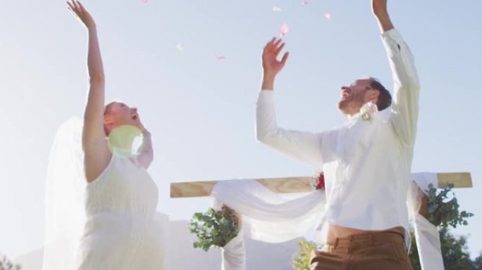 快乐的高加索新婚夫妇，在户外祭坛前跳着扔花瓣