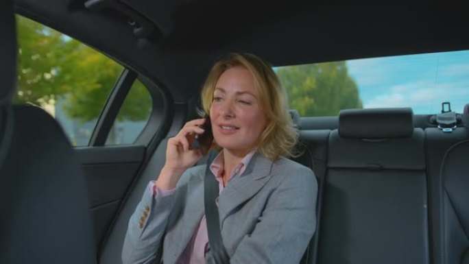 成熟的女商人坐在出租车或汽车的后座上，用手机聊天