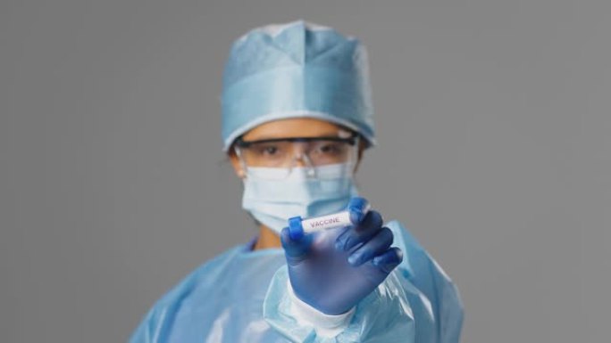 女性实验室研究人员穿着个人防护用品，手持标有疫苗的试管