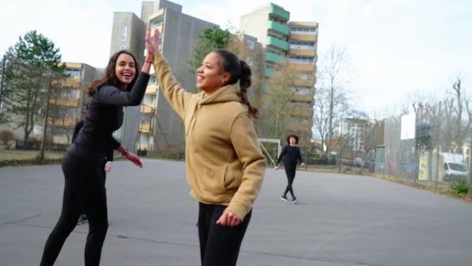 女子足球运动员向朋友击掌并在城市运动场庆祝进球