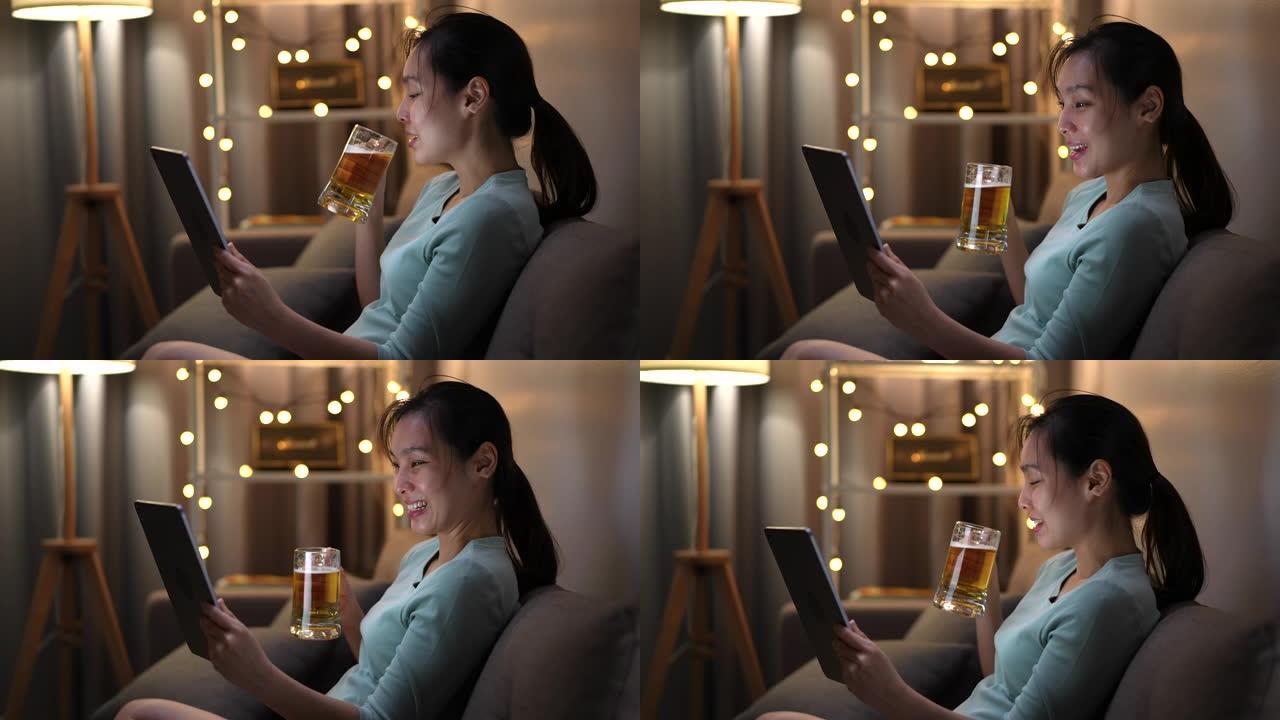 亚洲妇女与朋友进行视频电话会议，手里拿着啤酒做欢乐时光