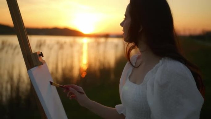 黄昏时，女艺术家在湖边的画布上绘画