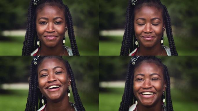 特写一位年轻黑人妇女在绿色公园里看着相机大笑的肖像。漂亮的女性，有着传统的非洲辫子和配饰，享受新鲜空