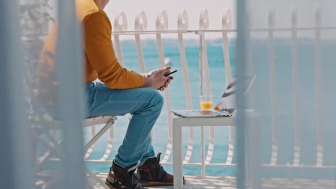 棕色短发的男人将智能手机中的信息输入到笔记本电脑中，向后倾斜并伸展双腿