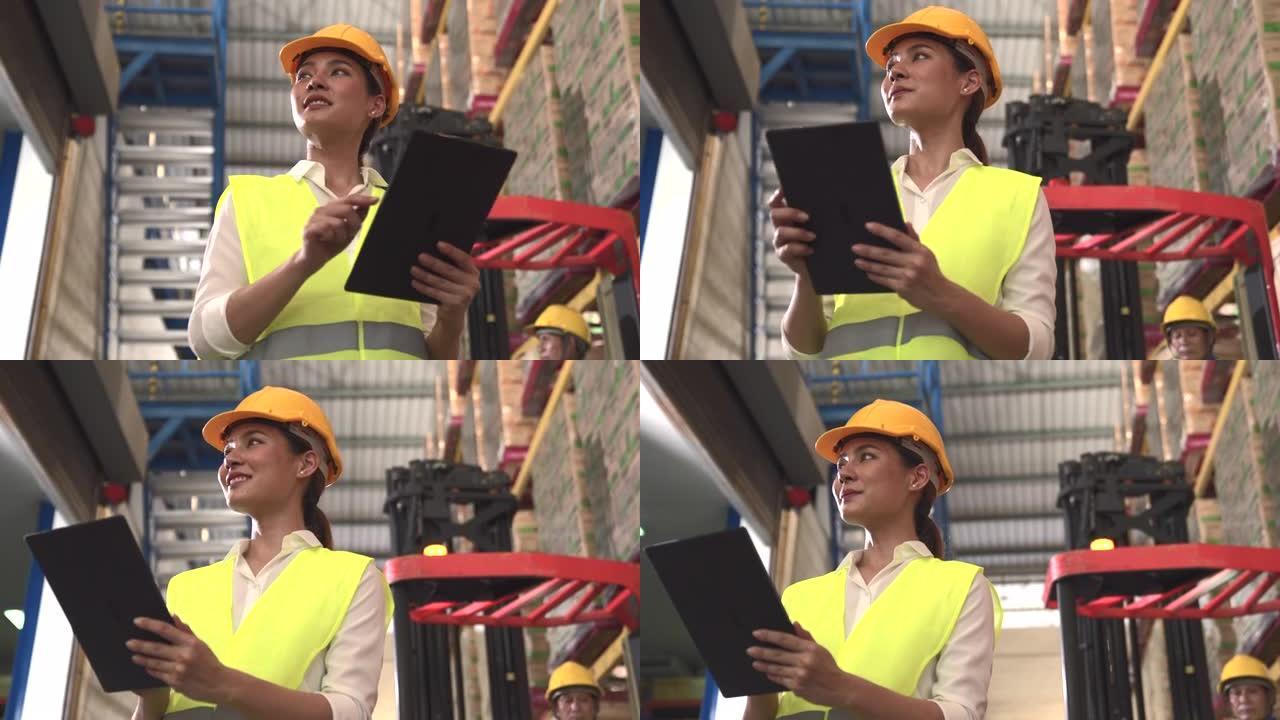 亚裔女工程师站在平板电脑上看着仓库货架。女人可以为男人工作，这意味着社会的平等。