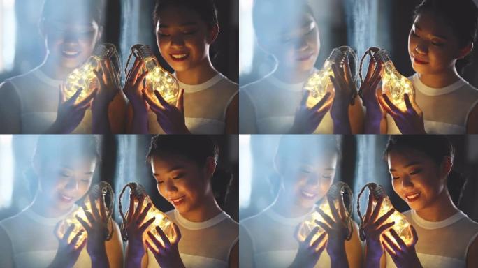 一个美丽的亚洲中国少女看着并拿着一个带发光二极管灯串的灯泡，用镜子反射微笑