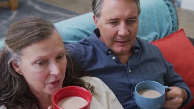 高年级白人夫妇坐在客厅的沙发上喝咖啡和聊天