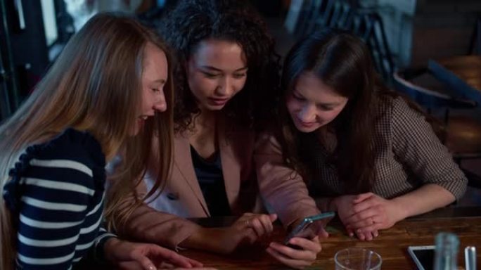 社交媒体概念。三个年轻美丽快乐的多民族女性朋友在咖啡店一起使用智能手机。