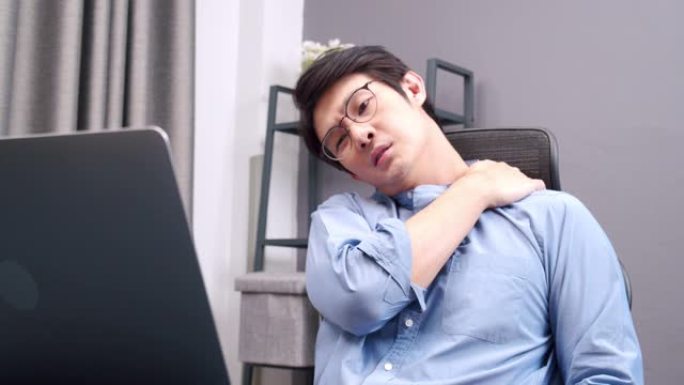 一整天坐在家里做生意的亚洲商人在笔记本电脑上工作，肩膀感到疼痛。肌肉疼痛，保健概念。