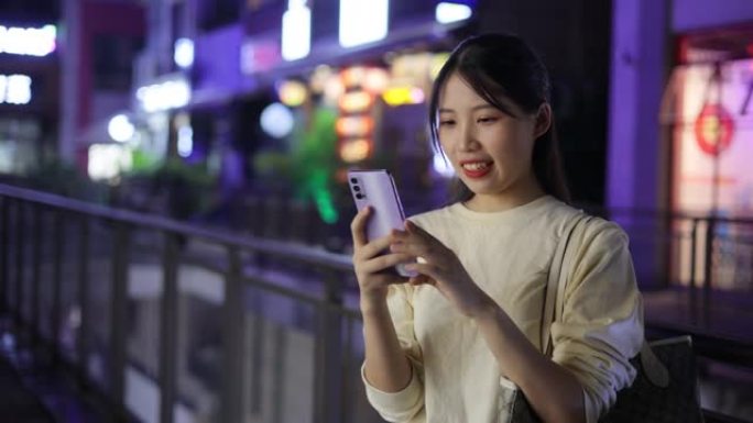 年轻的亚洲女性在夜间街头使用电话